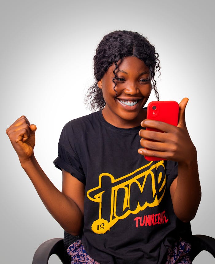 A cheerful woman celebrates success while looking at her smartphone, expressing happiness.